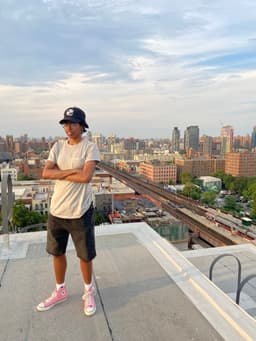 kidd stands with crossed arms on a rooftop in the day with a view of New York City behind her